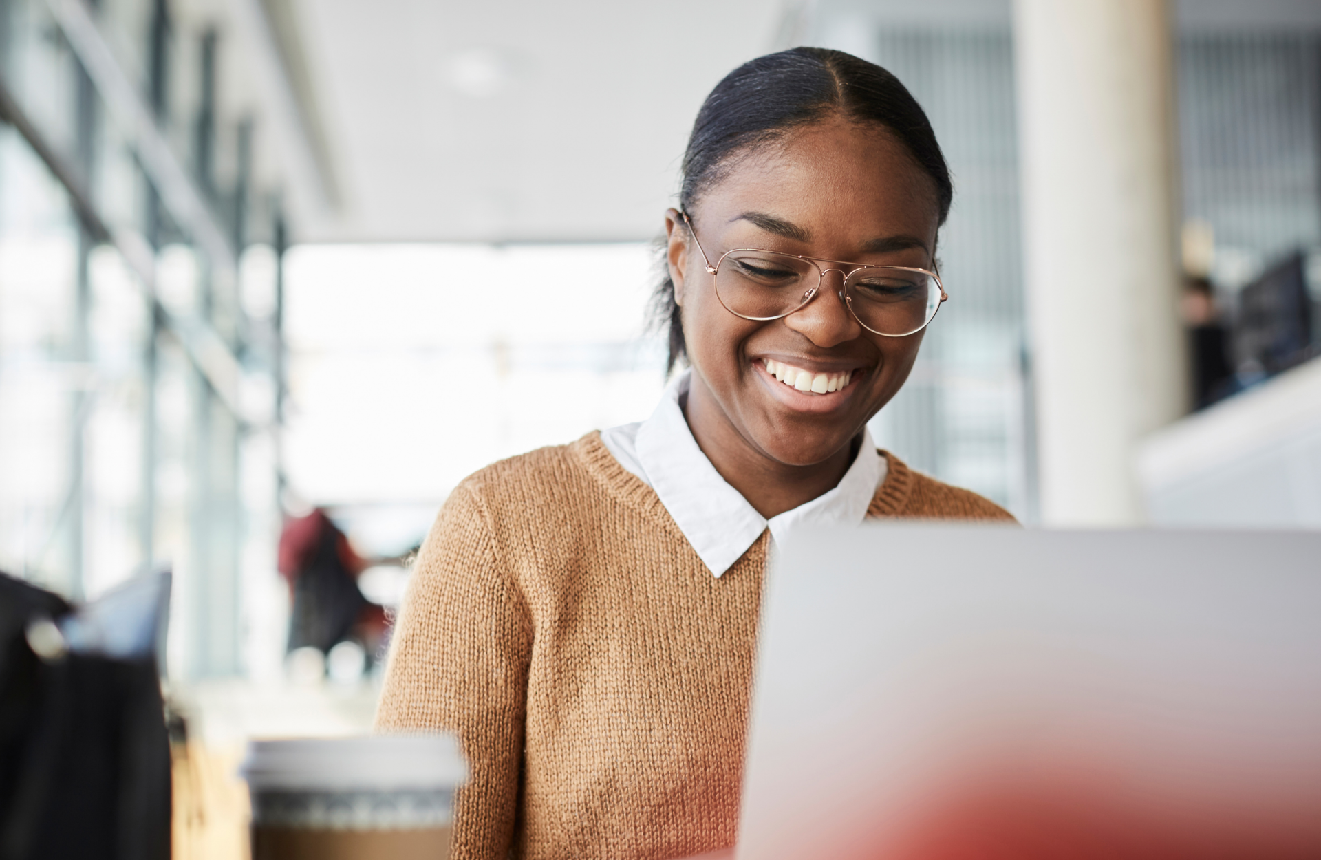 A woman wearing a beige sweater smiles while working on her laptop.