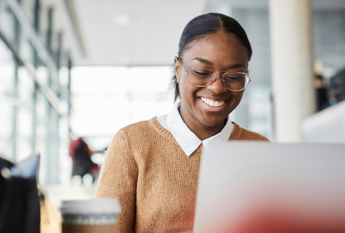 A woman wearing a beige sweater smiles while working on her laptop.