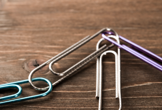 A closeup of four paperclips all clipped together on a wood table.