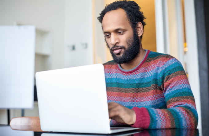 A man in a bright sweater works on a laptop in a meeting room.